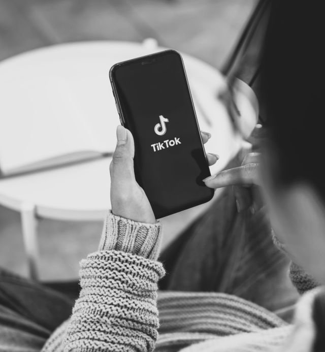 reseaux_sociaux_2B A close-up of a woman using the TikTok application on her iPhone while sitting on a couch at home.